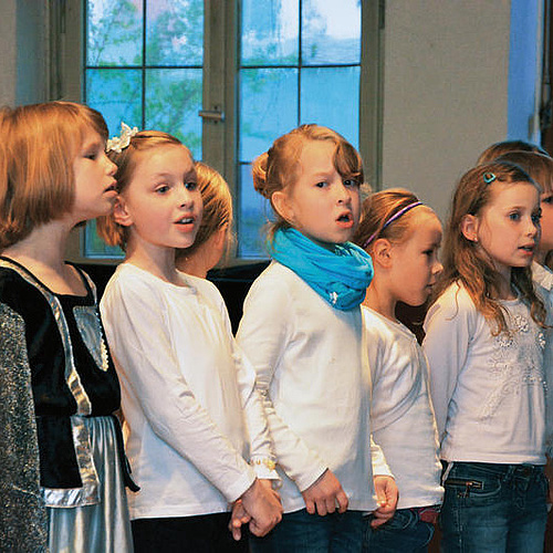 Grundschulkinder in weißen T-Shirts, ein Kind mit schwarzem Kleid, singen im Chor, 