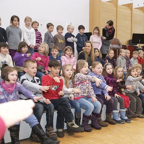 Große Gruppe von Grundschulkindern, die in einem Chor singen und dazu Gesten mit den Händen machen.