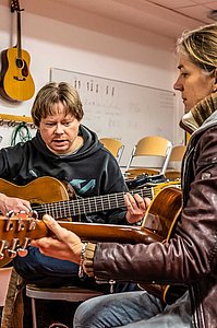Erwachsene Gitarrenschülerin und Gitarrenleher spielen gemeinsam in einem Musikraum