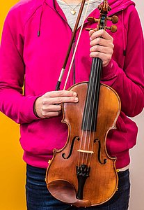Einer jugendliche Musikschülerin hält eine Violine vor ihrem Körper in den Händen