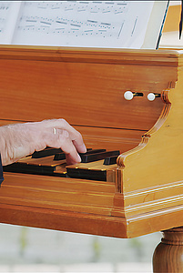 Detail der Klaviatur eines Cembalos aus hellem, warmtonigem Holz: eine Hand spielt einen Akkord in der hohen Lage.